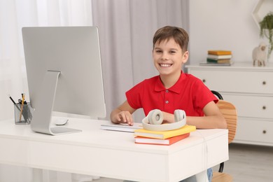 Photo of Boy using computer at desk in room. Home workplace