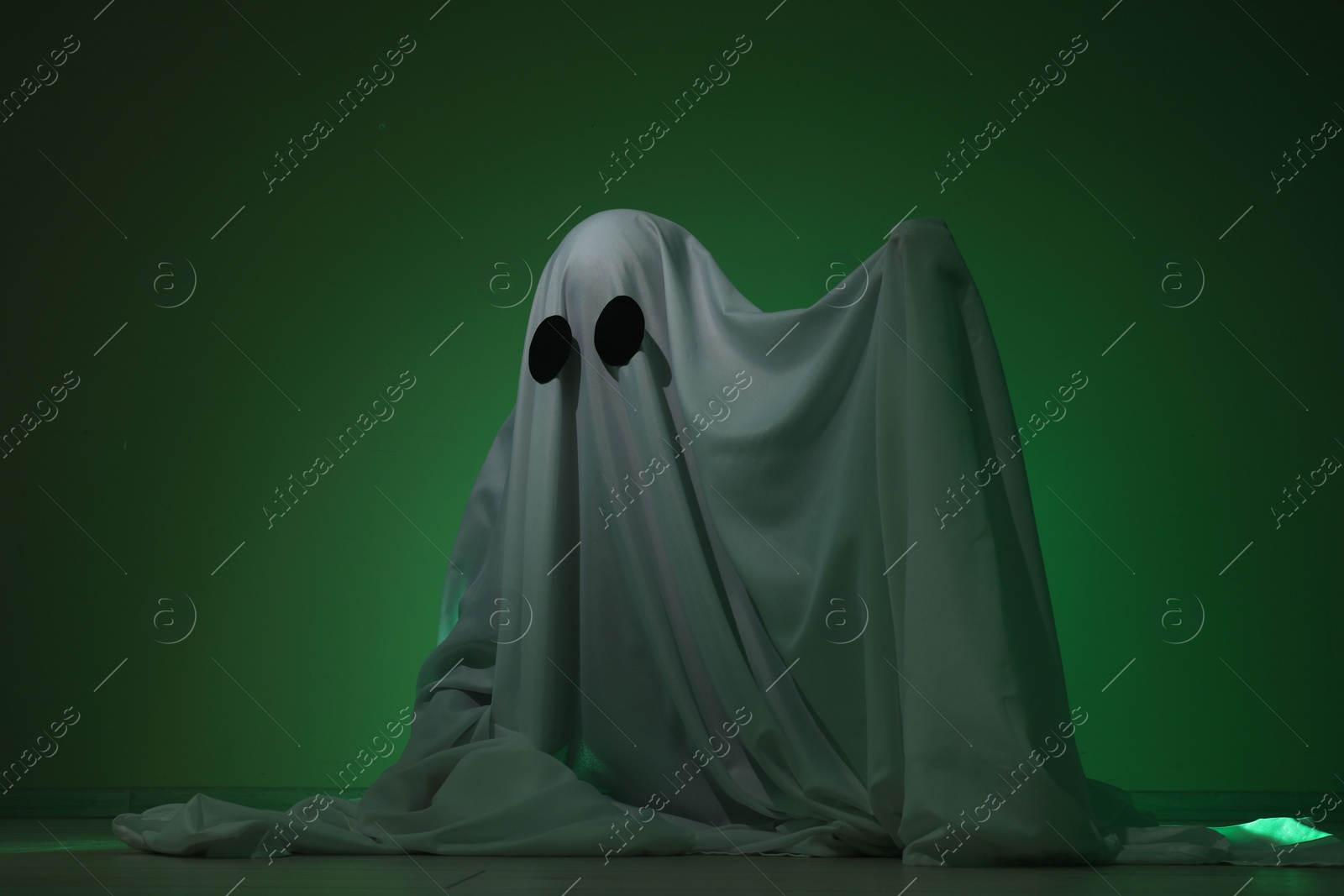 Photo of Creepy ghost. Woman covered with sheet in green light