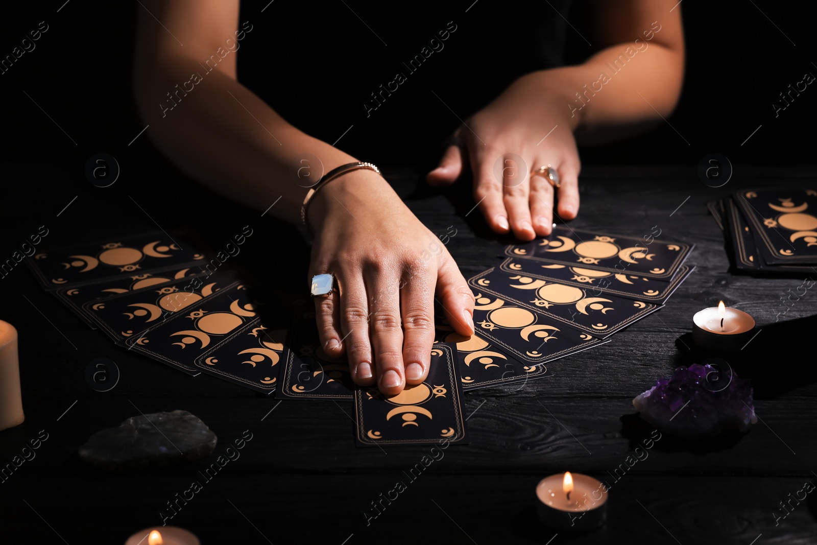 Photo of Soothsayer predicting future with tarot cards at table in darkness, closeup