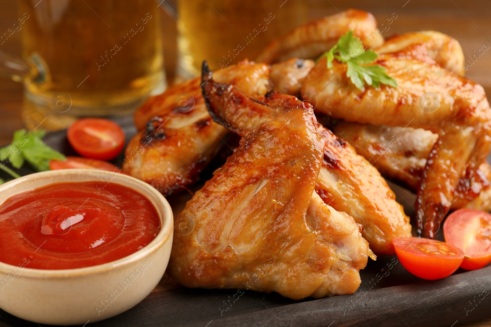 Photo of Delicious baked chicken wings, sauce and mugs with beer on table, closeup