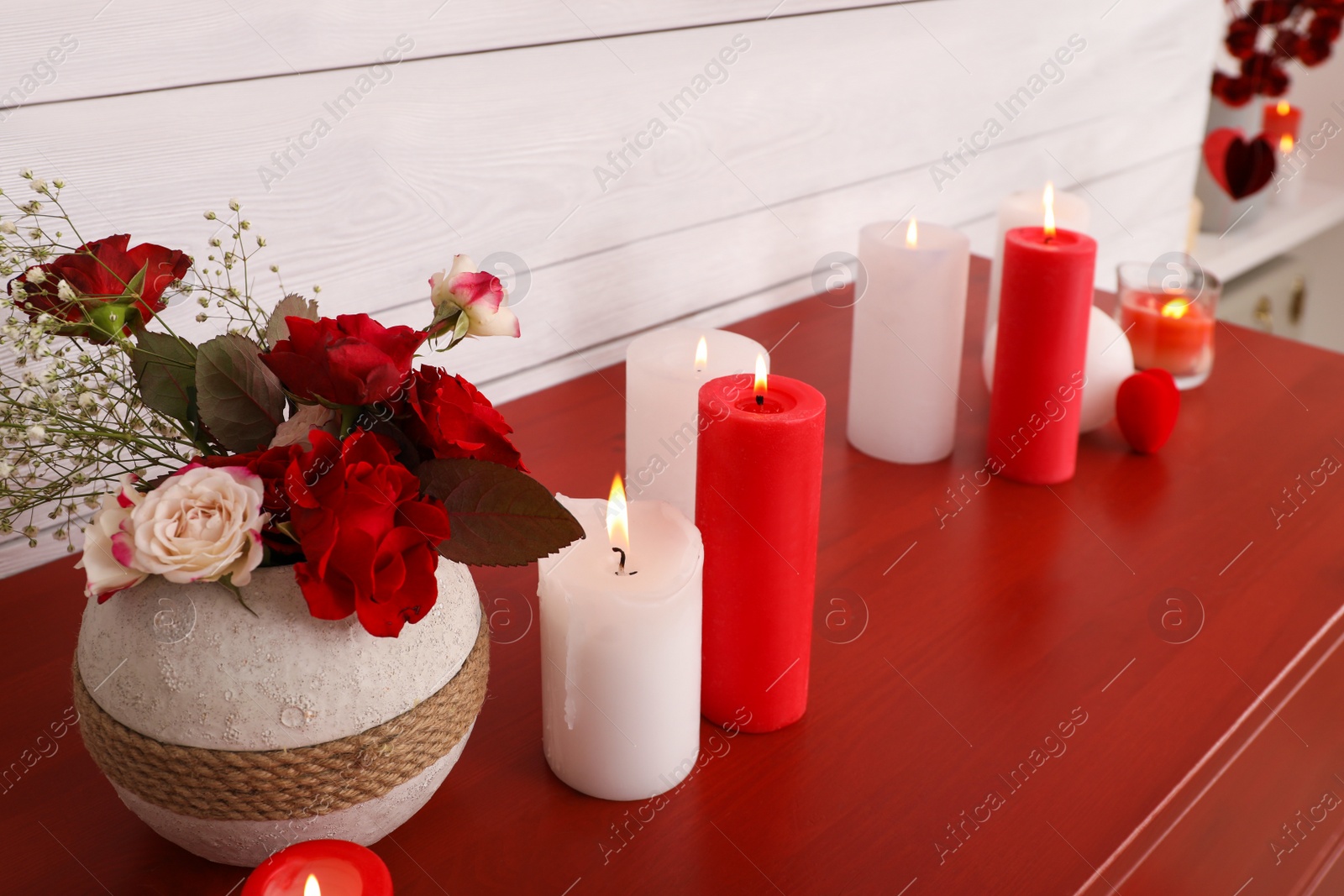 Photo of Burning candles and vase with flowers on red table indoors. Valentine's Day celebration