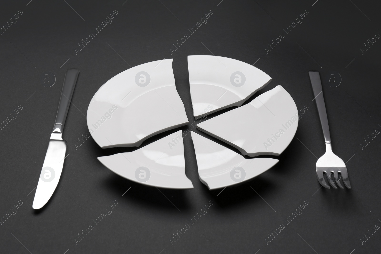 Photo of Pieces of broken ceramic plate and cutlery on dark grey background