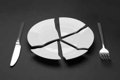 Pieces of broken ceramic plate and cutlery on dark grey background