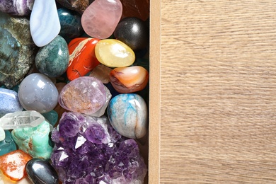 Box with different beautiful gemstones on wooden table, flat lay. Space for text