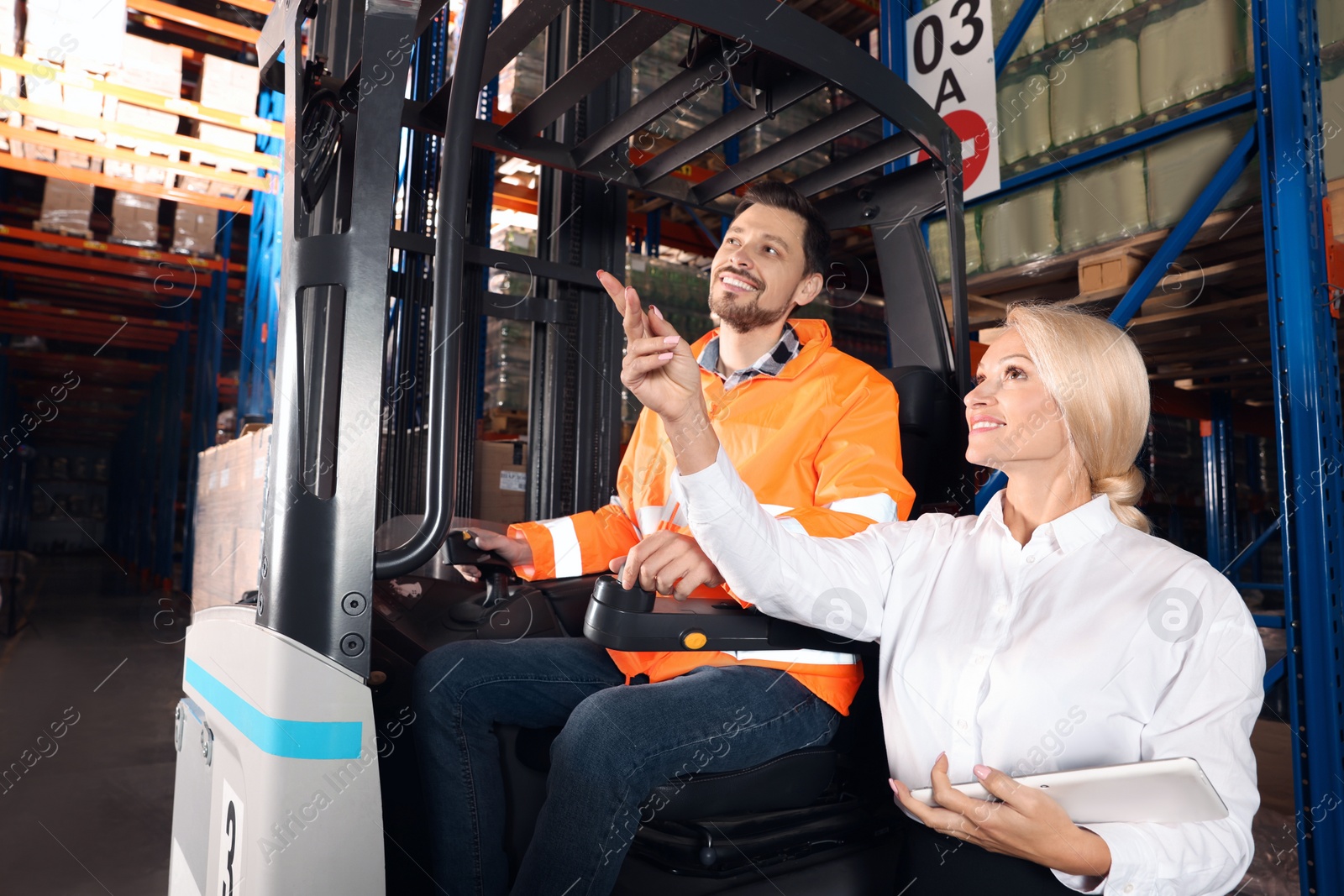 Photo of Happy worker talking with manager while sitting in forklift truck at warehouse