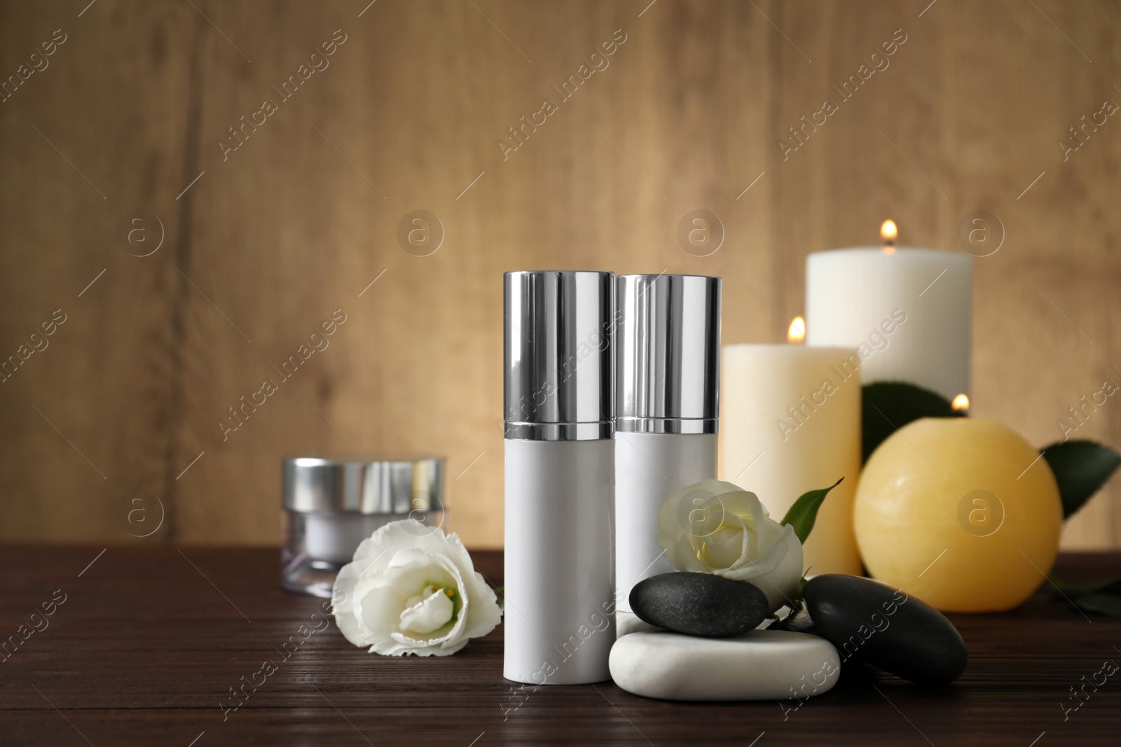 Photo of Composition with cosmetic products, spa stones and burning candles on wooden table. Space for text