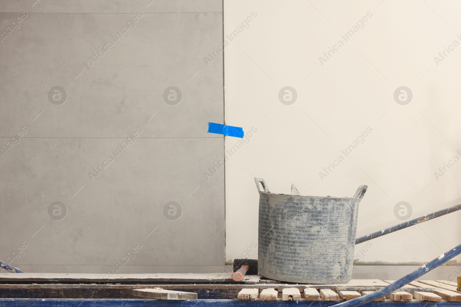 Photo of Different tools on tower tour near white wall with adhesive mix and tiles indoors