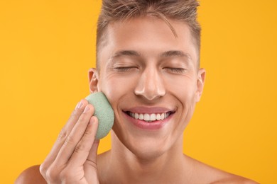Happy young man washing his face with sponge on orange background