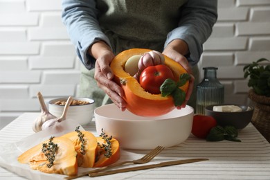 Woman putting pumpkin stuffed with different vegetables into baking dish at table, closeup