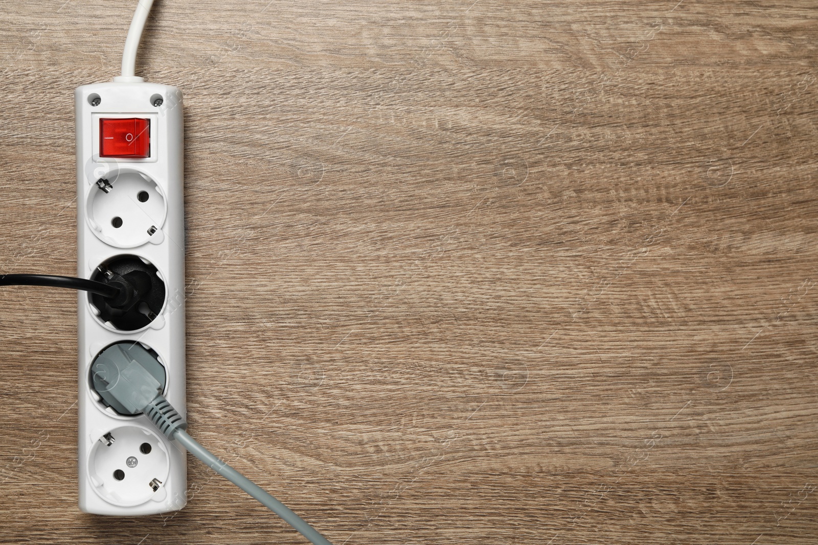 Photo of Power strip with extension cord on wooden floor, top view. Space for text