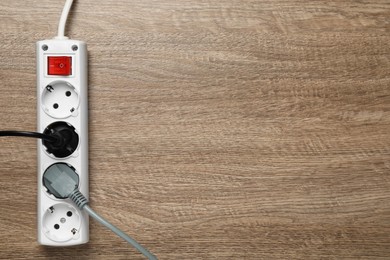 Power strip with extension cord on wooden floor, top view. Space for text