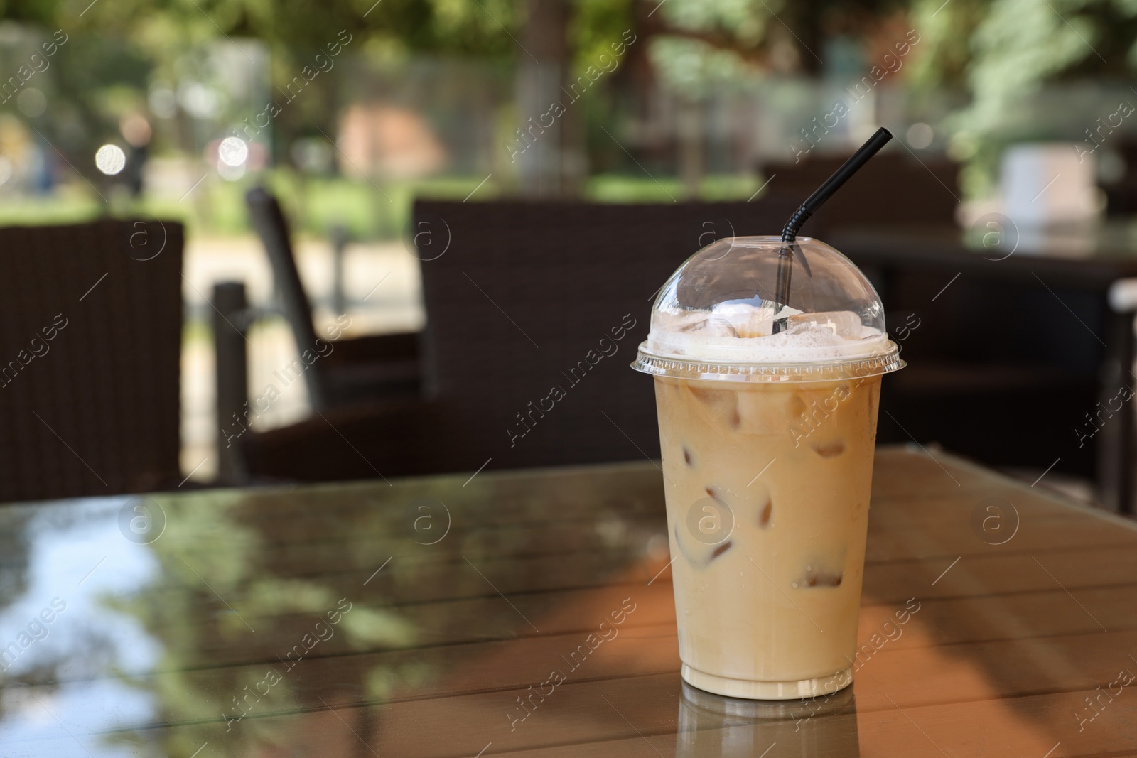 Photo of Plastic takeaway cup of delicious iced coffee on table in outdoor cafe, space for text