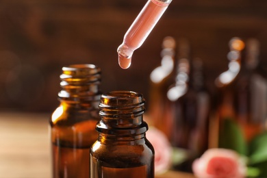 Photo of Dripping rose essential oil into bottle against blurred background