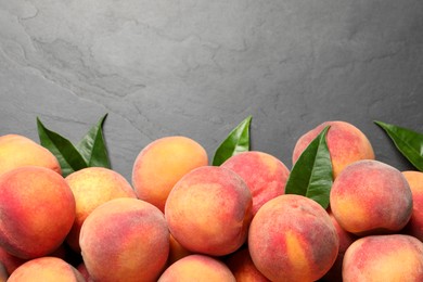Photo of Fresh peaches and leaves on dark grey textured table, flat lay. Space for text