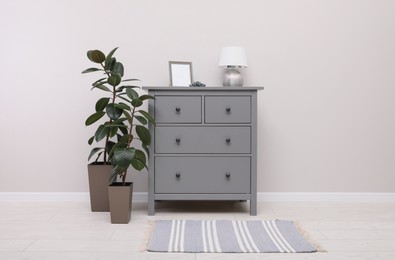 Photo of Stylish room interior with grey rug, chest of drawers and plants