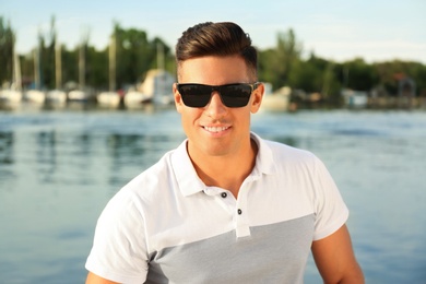 Handsome man wearing stylish sunglasses near river