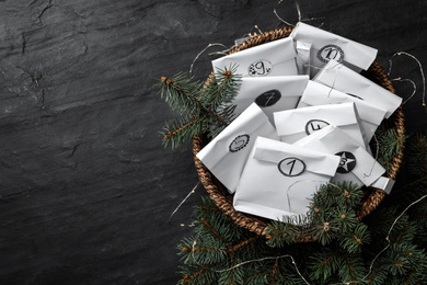 Photo of Paper bags, fir branches and garland on black table, flat lay with space for text. Christmas advent calendar