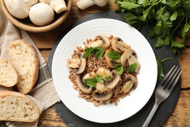 Tasty buckwheat with fresh parsley and mushrooms served on wooden table, flat lay