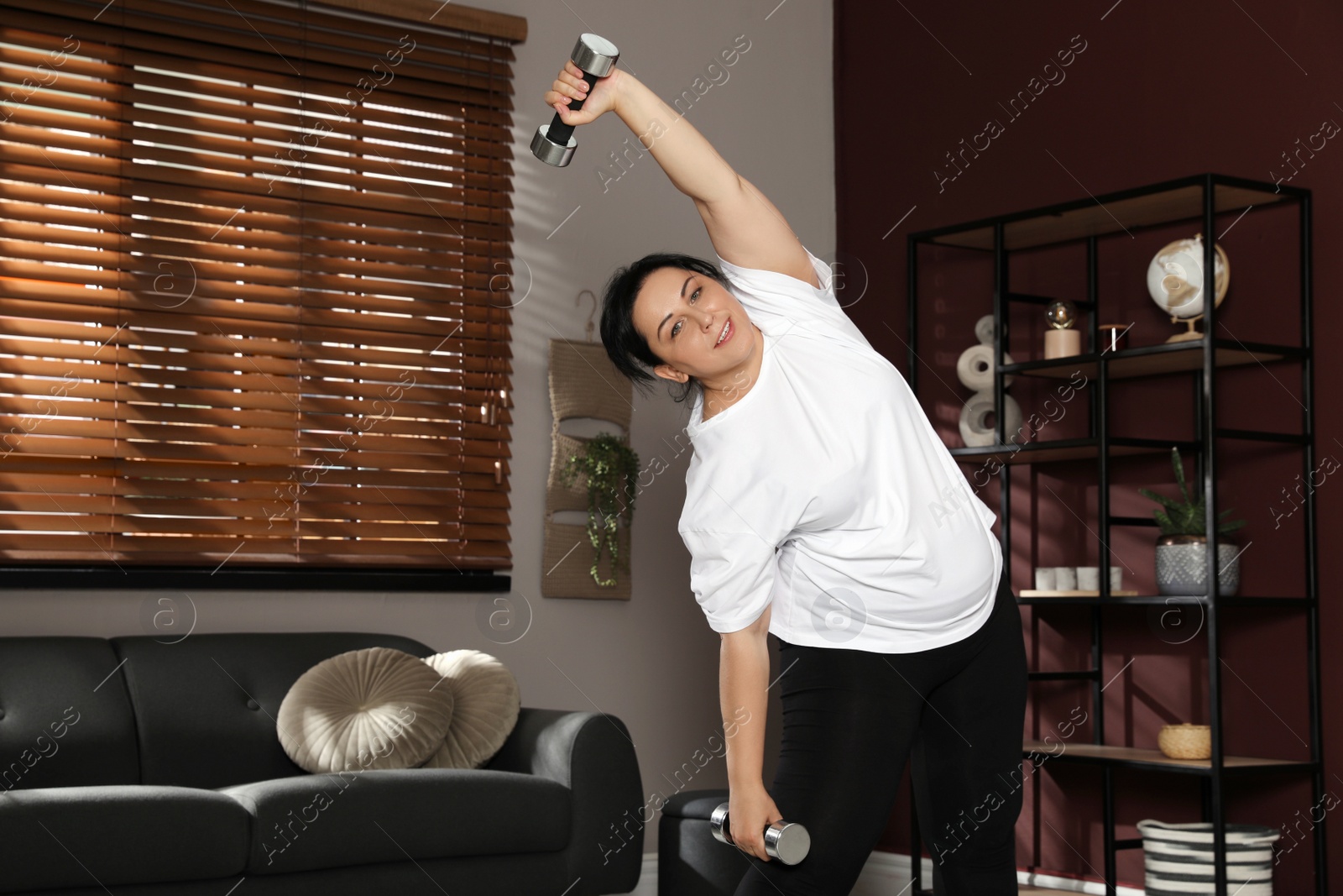 Photo of Overweight mature woman doing exercise with dumbbells at home