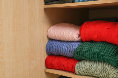 Different folded warm sweaters on wooden shelf