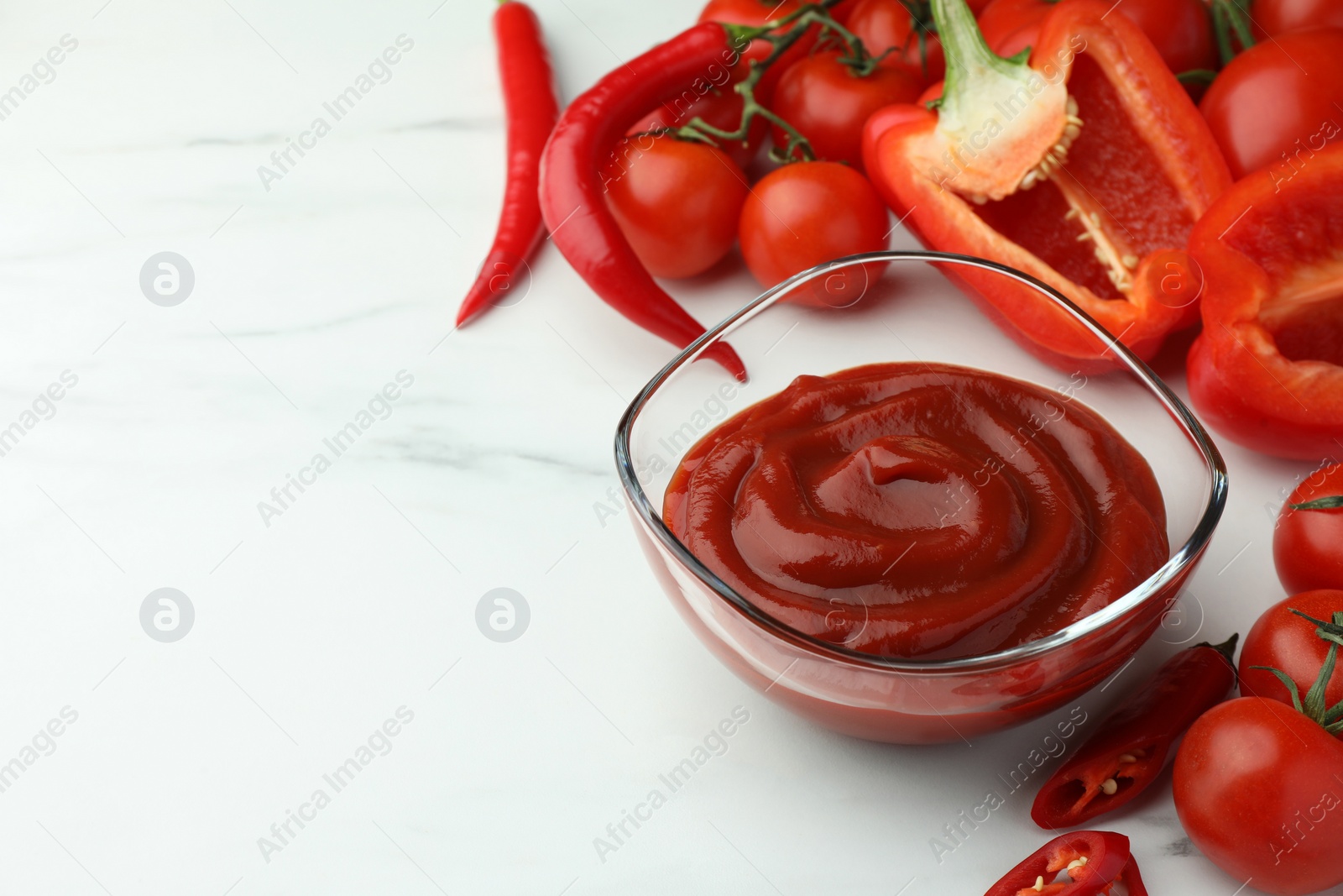 Photo of Bowl of tasty ketchup, tomatoes and peppers on white marble table, closeup. Space for text