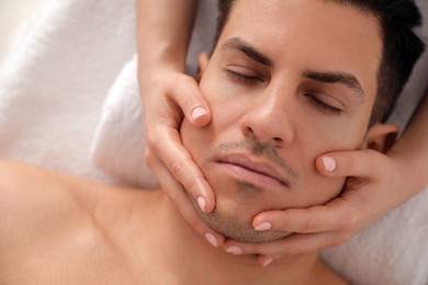 Photo of Man receiving facial massage in beauty salon, top view