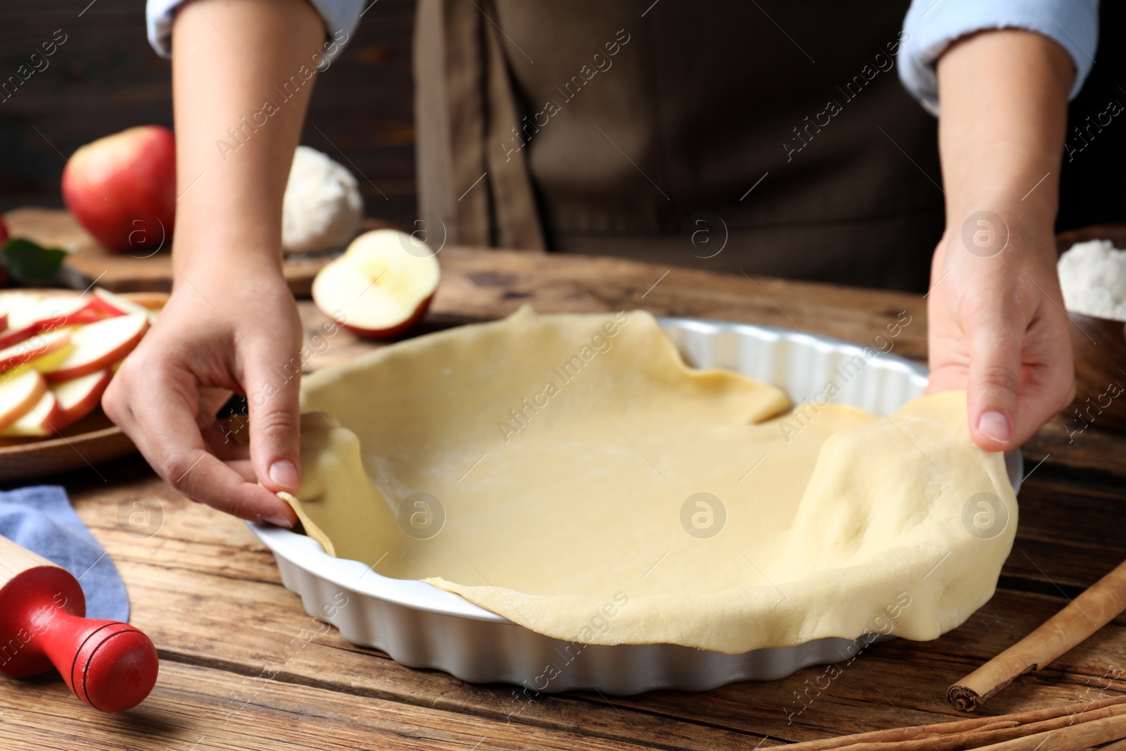 Photo of Woman putting dough for apple pie into baking dish at wooden table, closeup