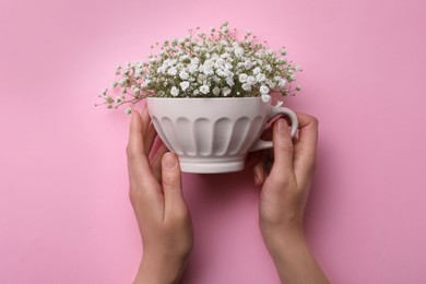 Photo of Top view of woman holding white cup with gypsophila on pink background, closeup