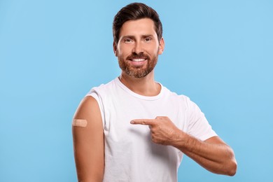 Photo of Man pointing at sticking plaster after vaccination on his arm against light blue background