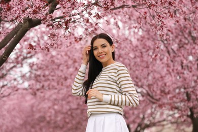 Pretty young woman in park with blooming trees. Spring look