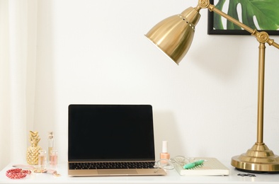 Photo of Stylish workplace with modern laptop and cosmetic products on table near light wall. Beauty blogger