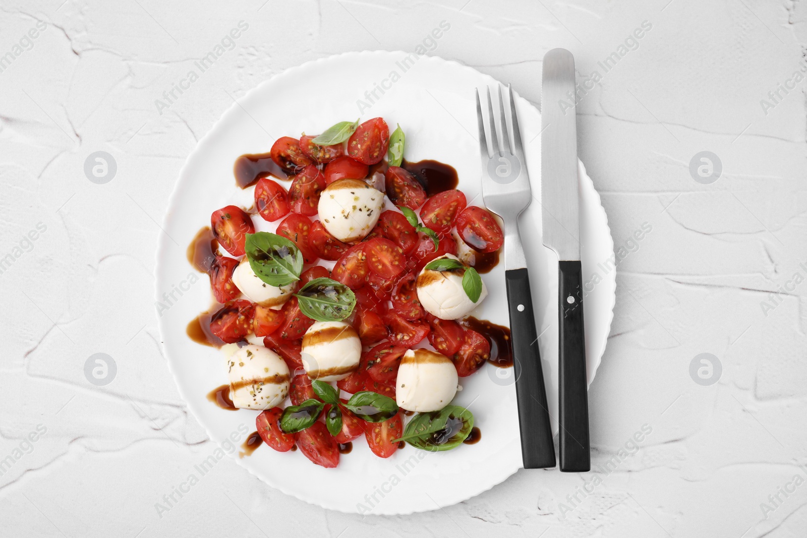 Photo of Tasty salad Caprese with tomatoes, mozzarella balls, basil and cutlery on white textured table, top view