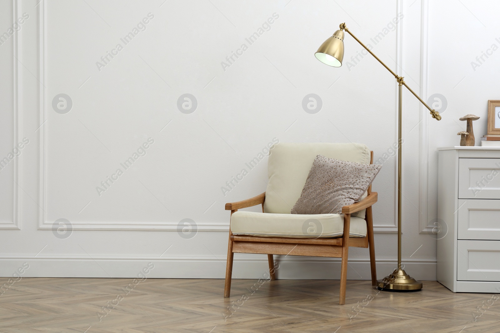 Photo of Stylish room interior with lamp, chest of drawers and armchair near white wall. Space for text