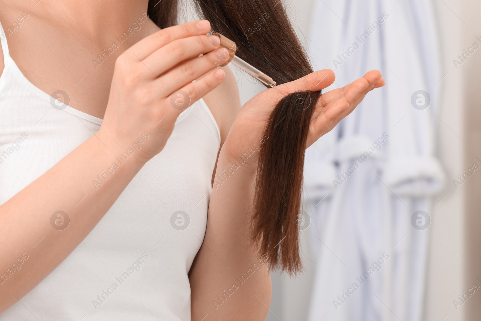 Photo of Woman applying essential oil onto hair on blurred background, closeup