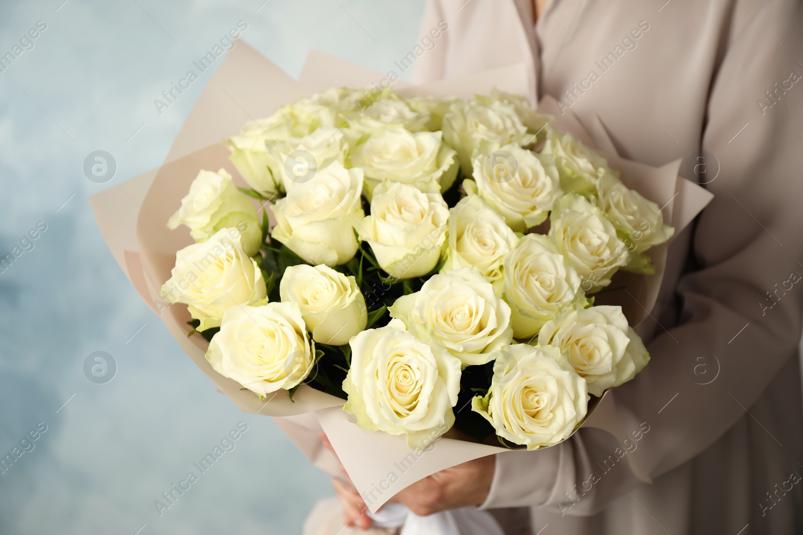 Photo of Woman holding luxury bouquet of fresh roses on light blue background, closeup