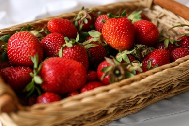 Photo of Wicker basket with ripe strawberries and napkin on white table, closeup