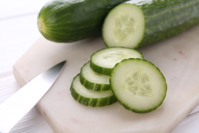 Photo of Cucumbers, knife and marble cutting board on white table, closeup