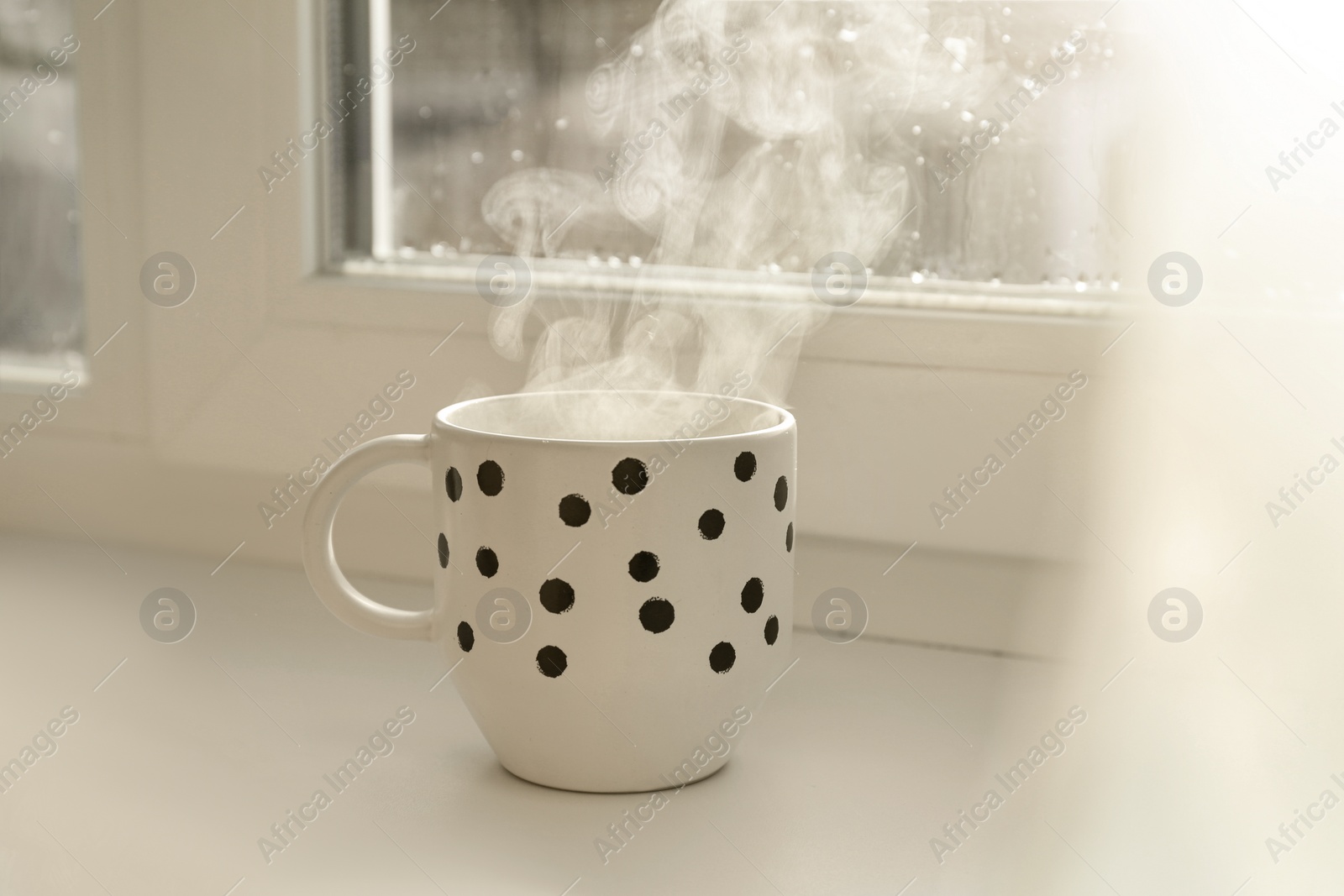 Photo of Cup of hot drink near window on rainy day