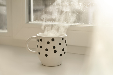 Cup of hot drink near window on rainy day