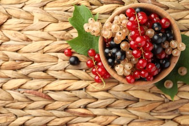 Photo of Different fresh ripe currants and green leaves on wicker surface, flat lay. Space for text