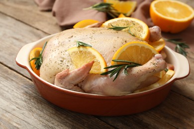 Photo of Chicken with orange slices and rosemary in baking pan on wooden table