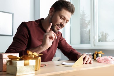 Man writing message in greeting card at wooden table in room