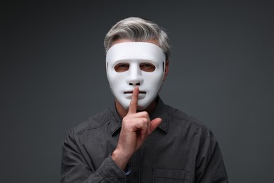 Photo of Man in mask showing hush gesture against dark grey background