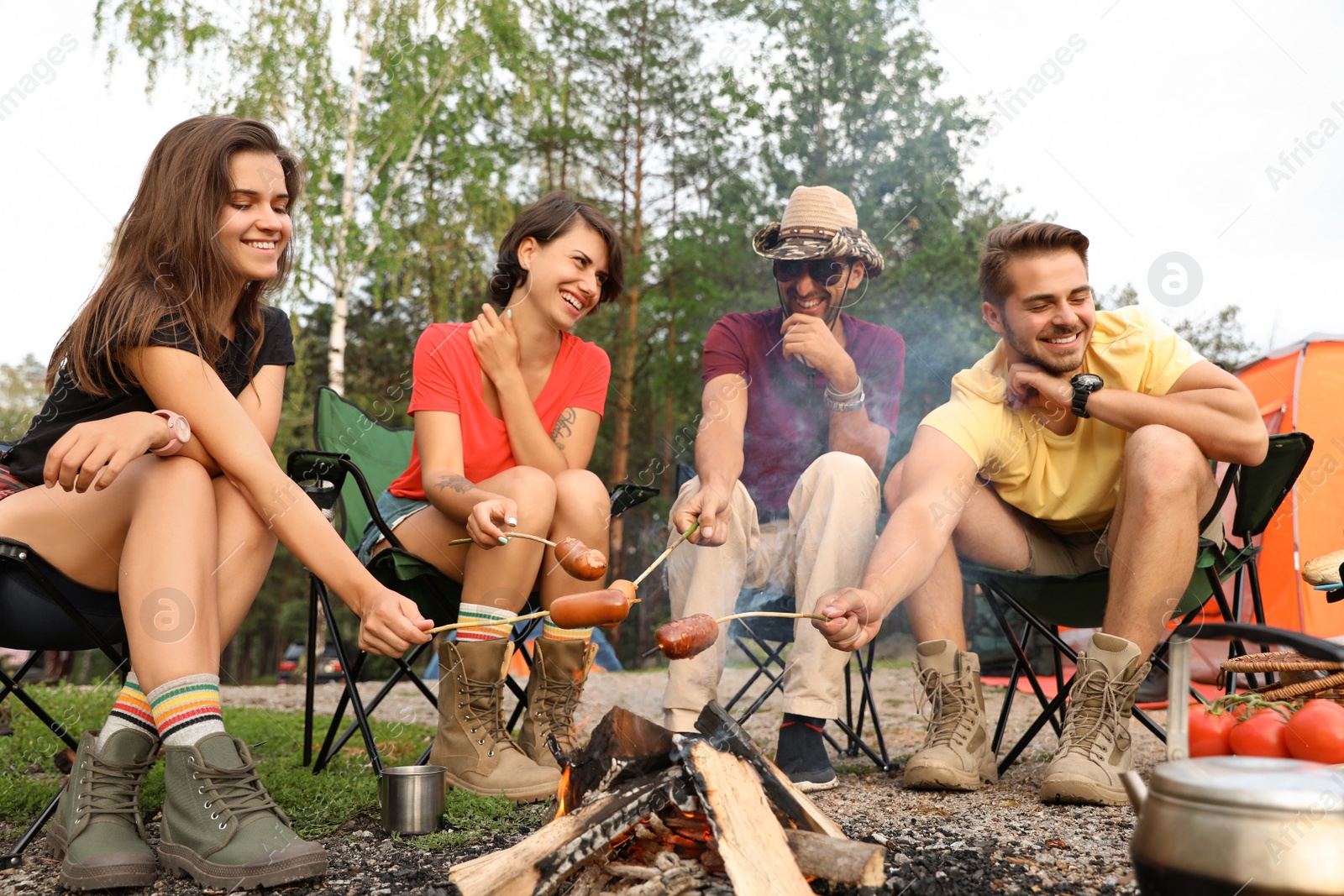 Photo of People having lunch with sausages near camping tent outdoors