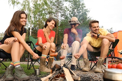 People having lunch with sausages near camping tent outdoors