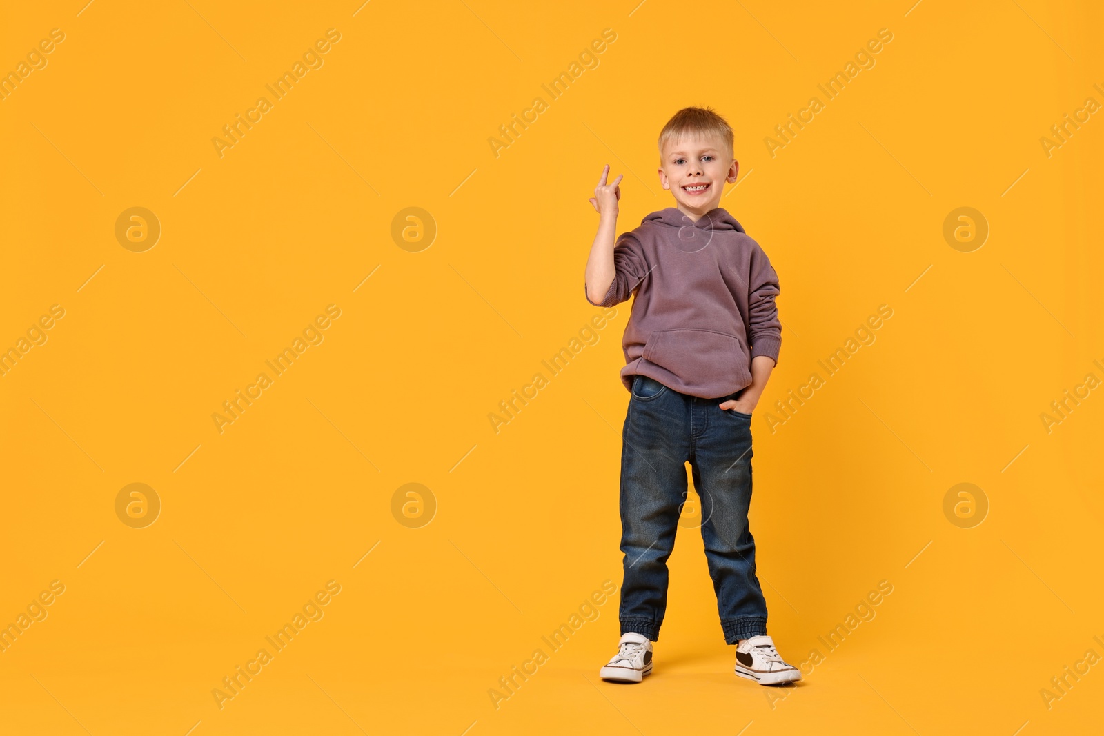 Photo of Happy little boy dancing on yellow background. Space for text