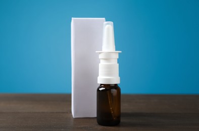Photo of Nasal spray and package on wooden table against light blue background