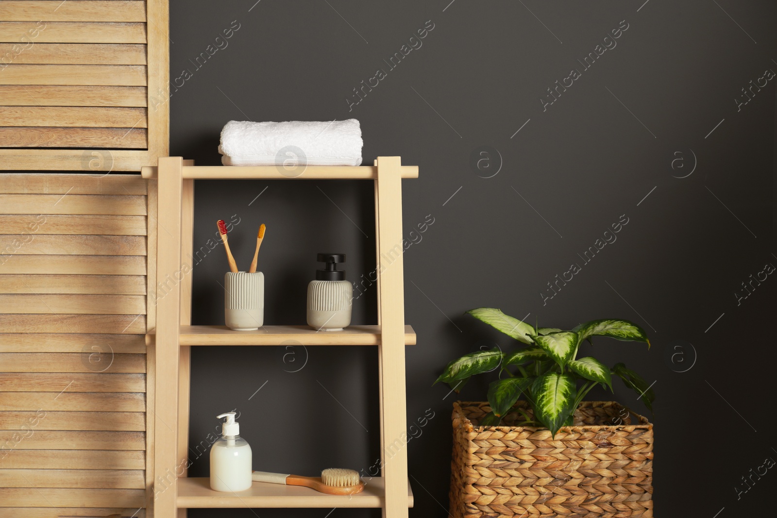 Photo of Wooden shelving unit with toiletries near black wall indoors. Bathroom interior element