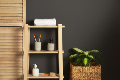Wooden shelving unit with toiletries near black wall indoors. Bathroom interior element
