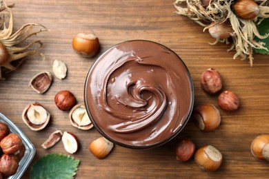 Tasty chocolate hazelnut spread and nuts on wooden table, flat lay